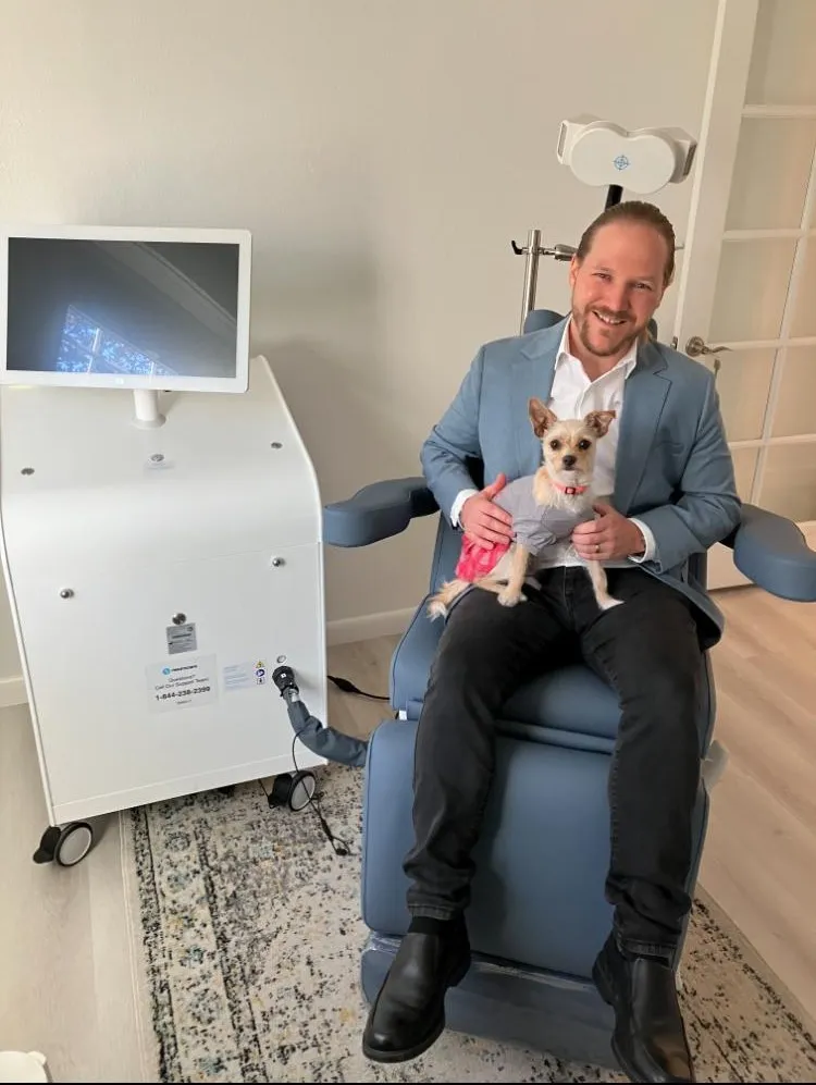 Dr. Karan Narwal holding a dog in a medical treatment chair next to TMS equipment